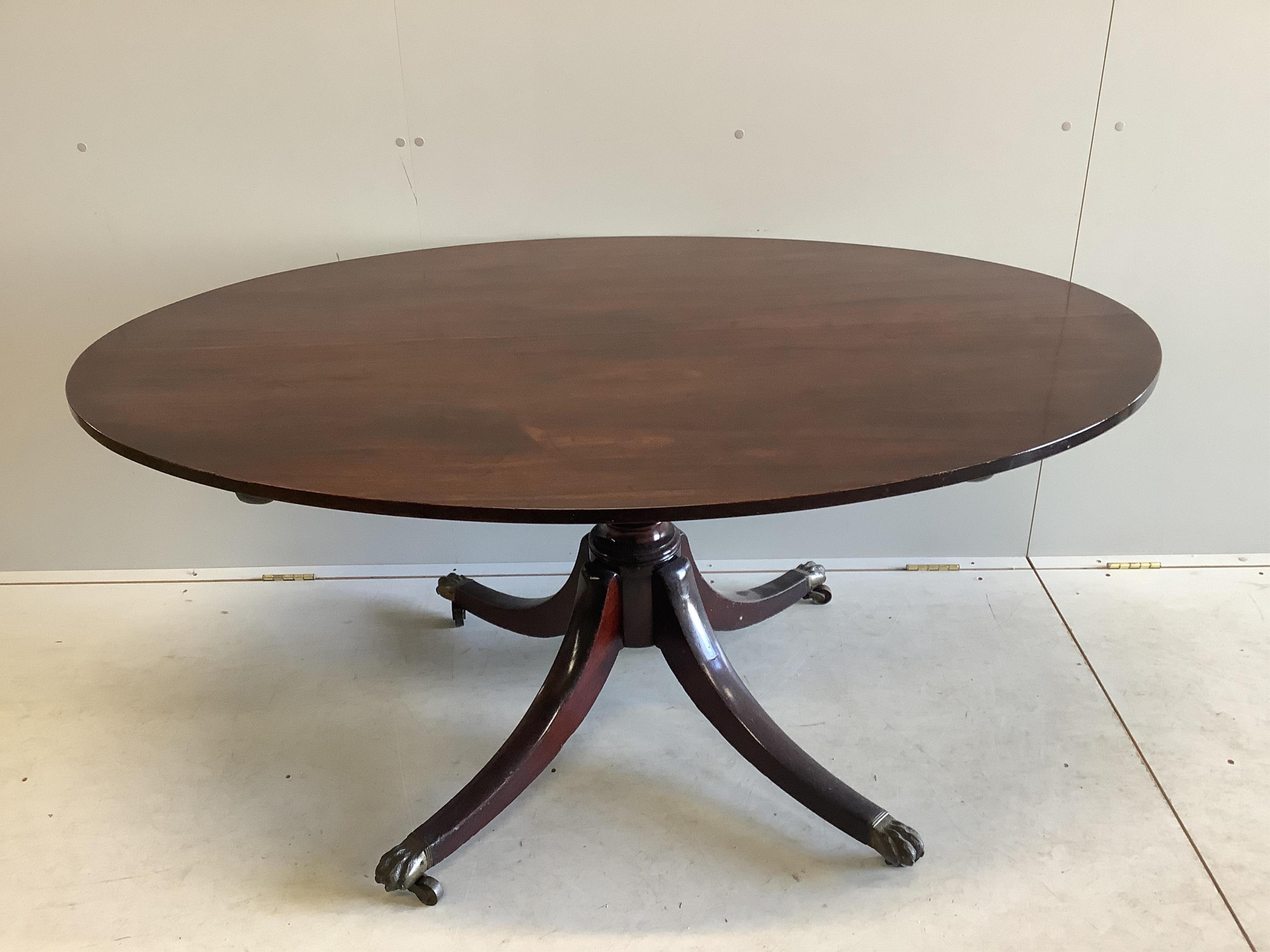 A George III mahogany oval pedestal dining table with brass claw feet, width 152cm, depth 105cm, height 71cm, together with a set of six Regency mahogany sabre leg dining chairs. Condition - fair to good